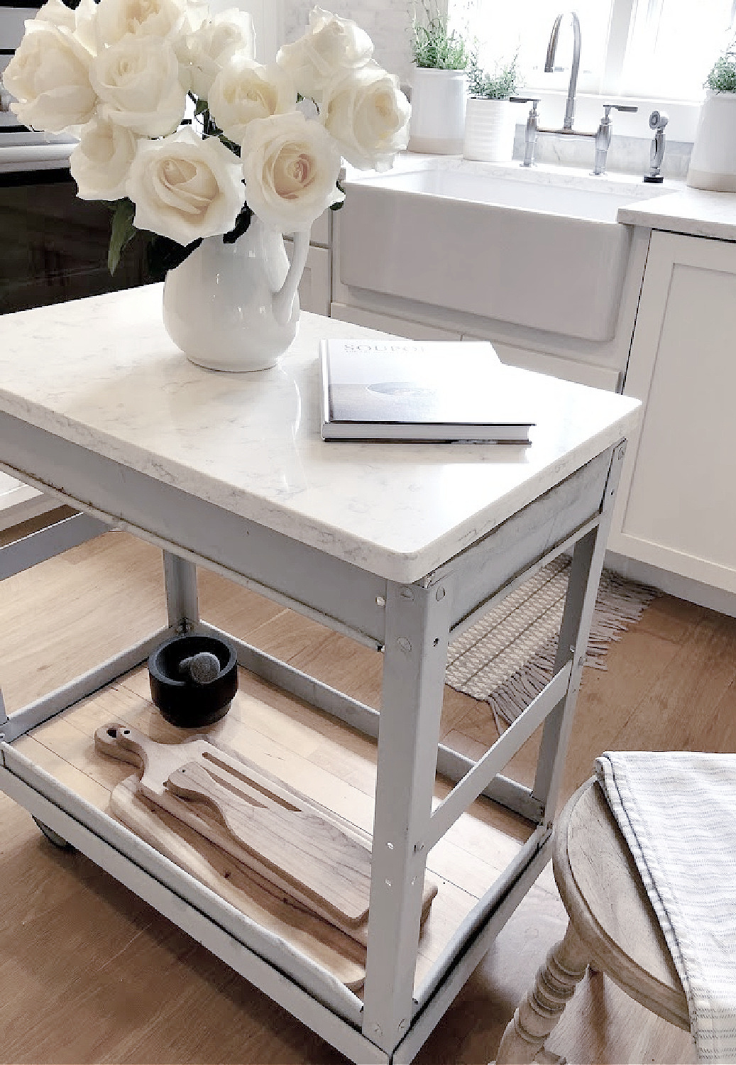 White roses in vintage ironstone pitcher on an industrial steel cart in my serene white kitchen - Hello Lovely. #whitekitchens #modernfrench #farmhousekitchen