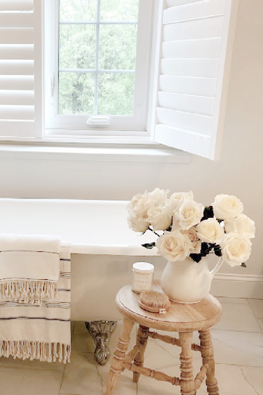 Modern French white bathroom with clawfoot tub, white roses, Turkish towels, and rustic wood stool - Hello Lovely Studio.