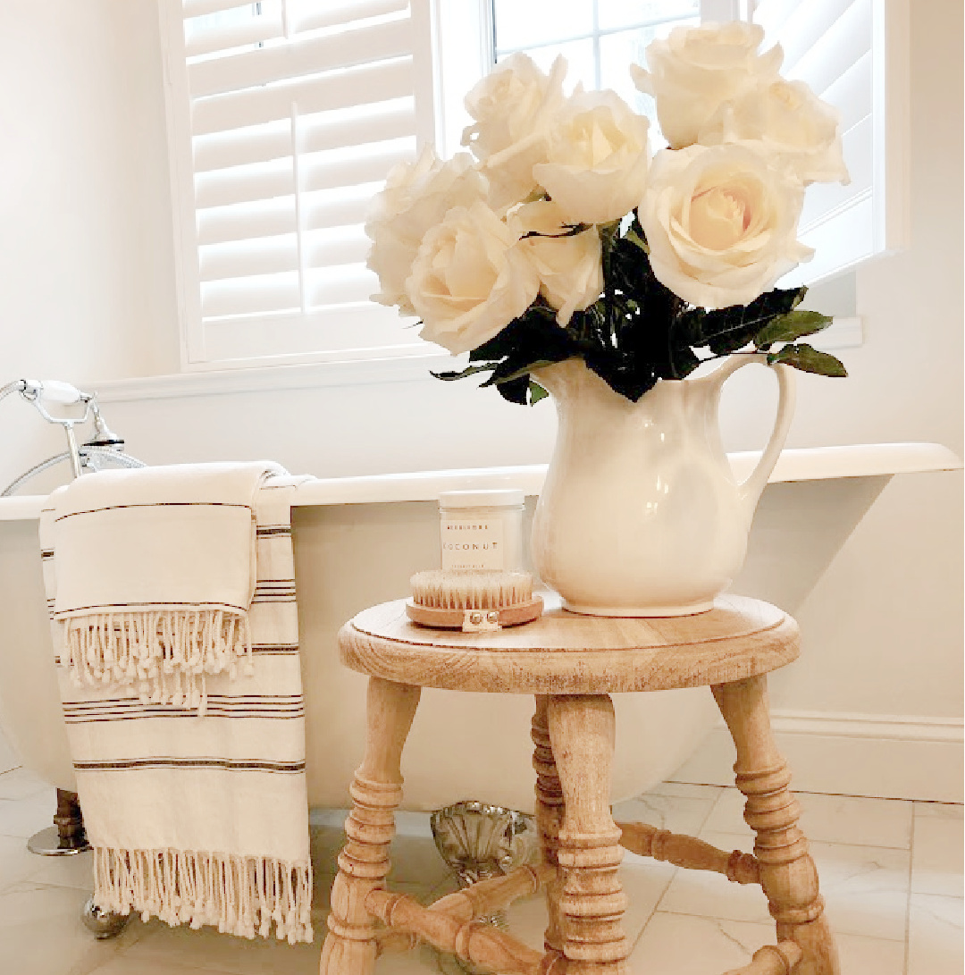 White roses in ironstone vintage pitcher on farm stool with clawfoot tub - Hello Lovely Studio.