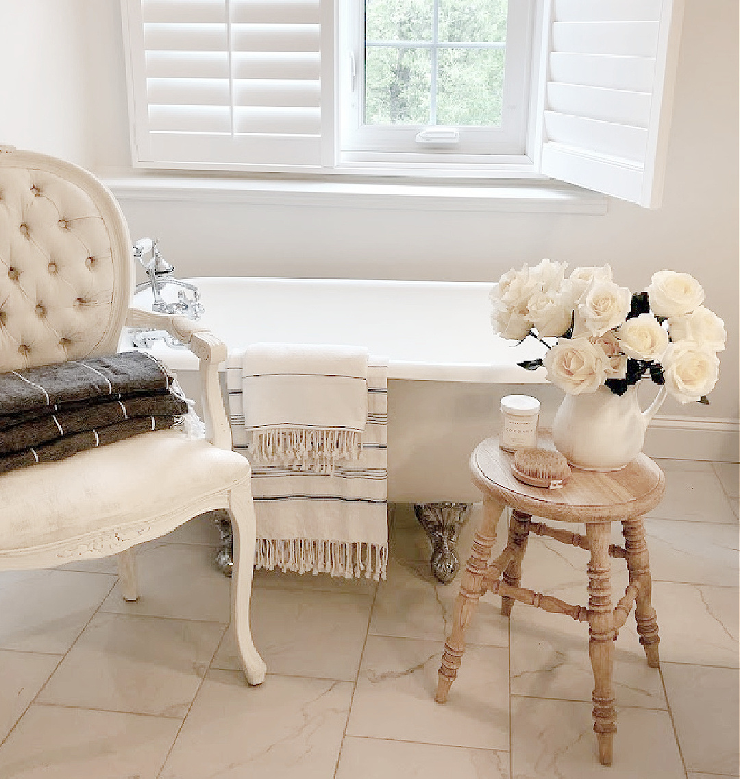 Serene white bath with vintage clawfoot tub and Louis style chair - Hello Lovely Studio. #modernfrench