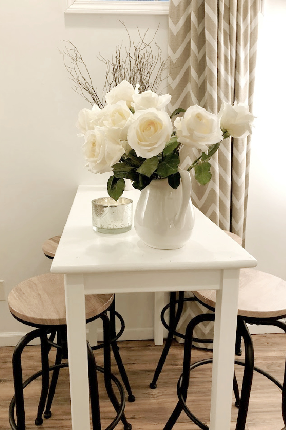 White roses in ironstone pitcher on pub table with industrial stools - Hello Lovely.