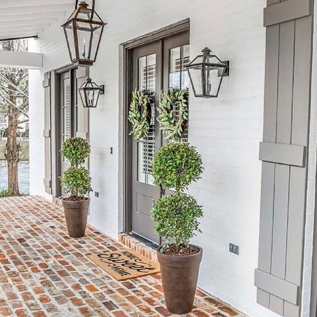 SW Snowbound 7004 white painted brick exterior with medium gray shutters, topiaries, and brick floor. @brandiolivarealty #swsnowbound #whitebrickfacade