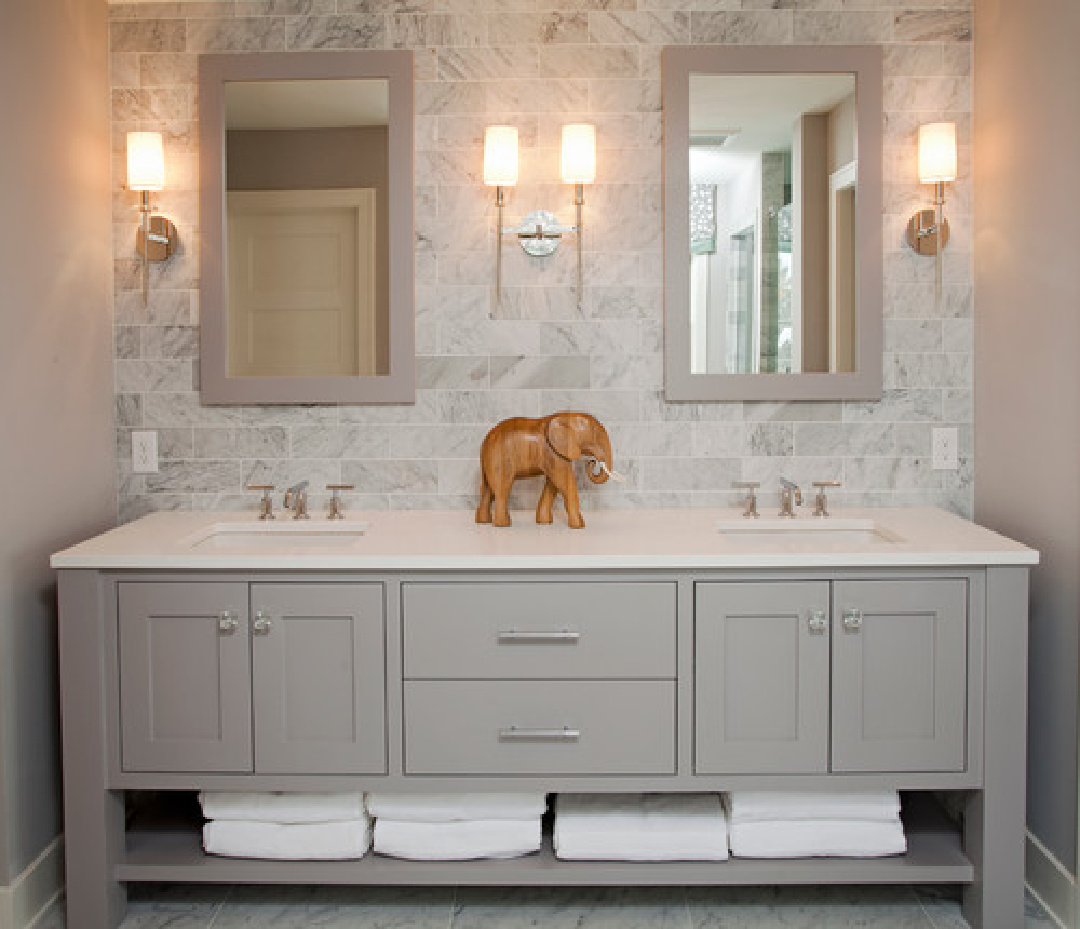 Grey painted double bath vanity with marble subway tile and wall sconces.