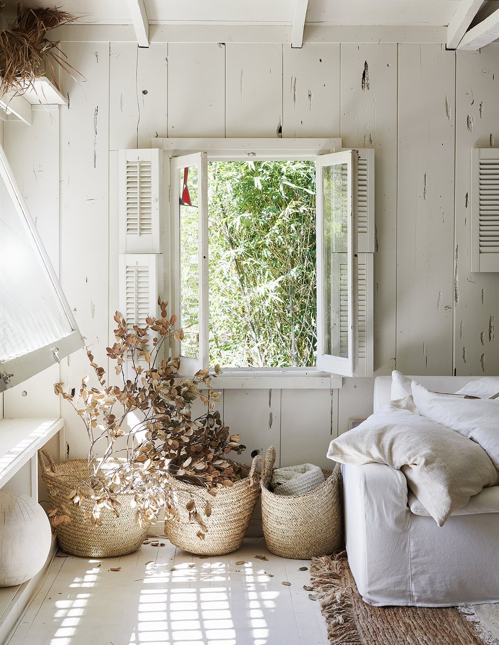 White painted floors, seagrass Frnech baskets, white slipcovered sofa, and natural fiber rugs in a modern rustic California cottage designed by Leanne Ford (photo by Amy Neunsinger).