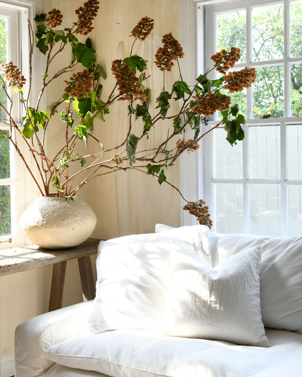 Leanne Ford designed living room with walls rubbed with coffee, a mix of pieced together flooring, white slipcovered sofa, and rustic organic modern style - photo by Erin Kelly.