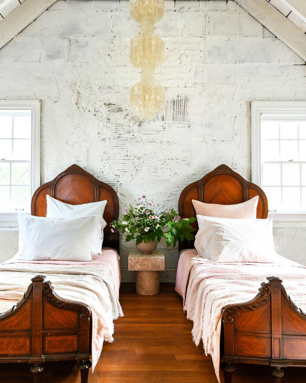 Leanne Ford designed bedroom. Twin antique beds in a rustic vintage bedroom with rough textured white walls and wood floors - photo by Erin Kelly.