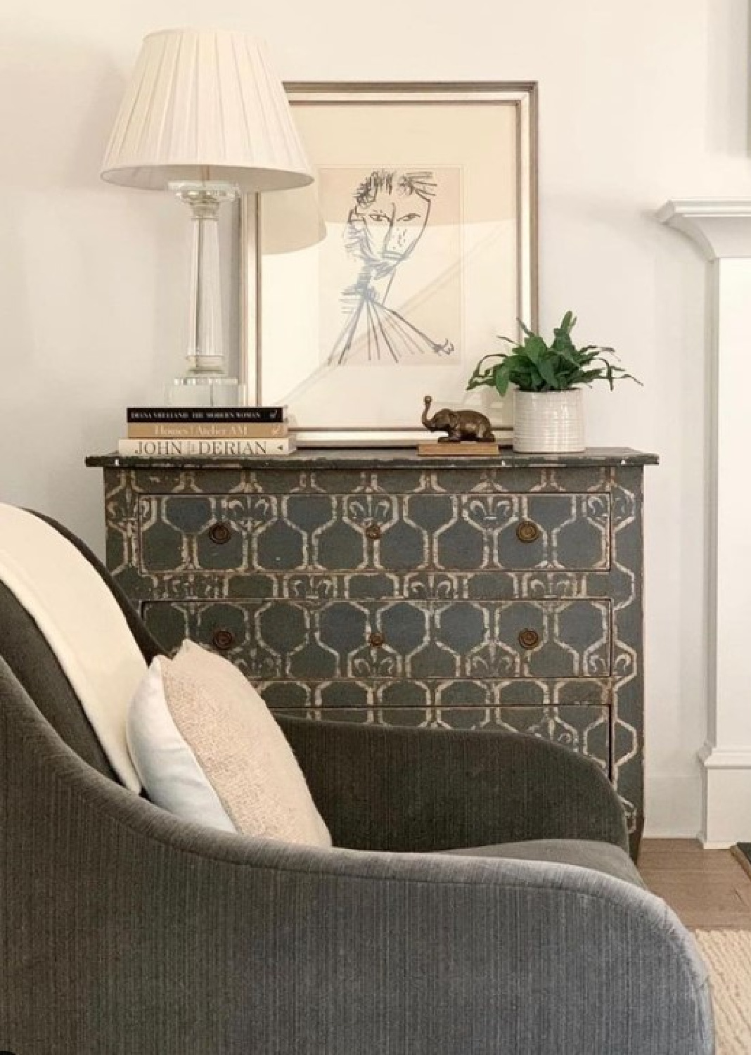 Deep grey stenciled chest and curvy sumptuous upholstered chair in a living area designed by Sherry Hart.
