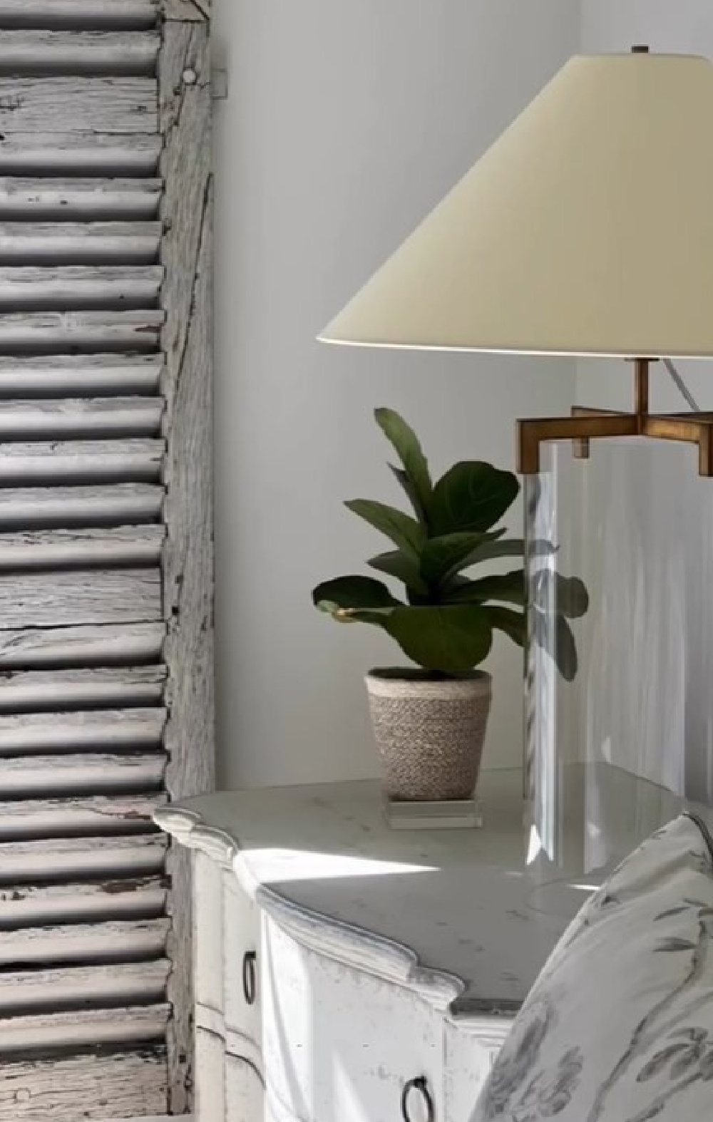 Rustic light grey shutter near a bedside table with beautiful Visual Comfort lamp in a bedroom designed by Sherry Hart.