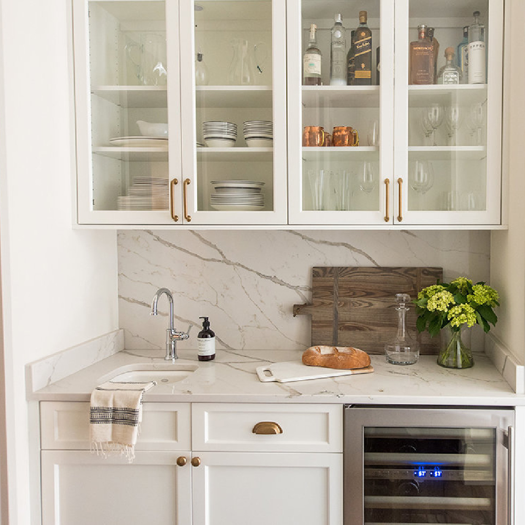 Beautiful beverage station area in a white kitchen designed by Whittney Parkinson with glass front upper cabinets. #whitekitchens
