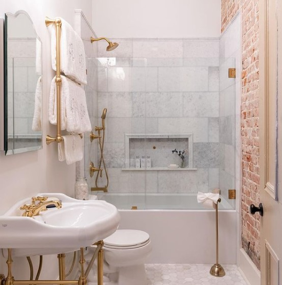 Beautiful renovated bath with Chantilly Lace paint color, marble floor, console sink, exposed brick wall, and brass hardware - @fisherkellyrenovations