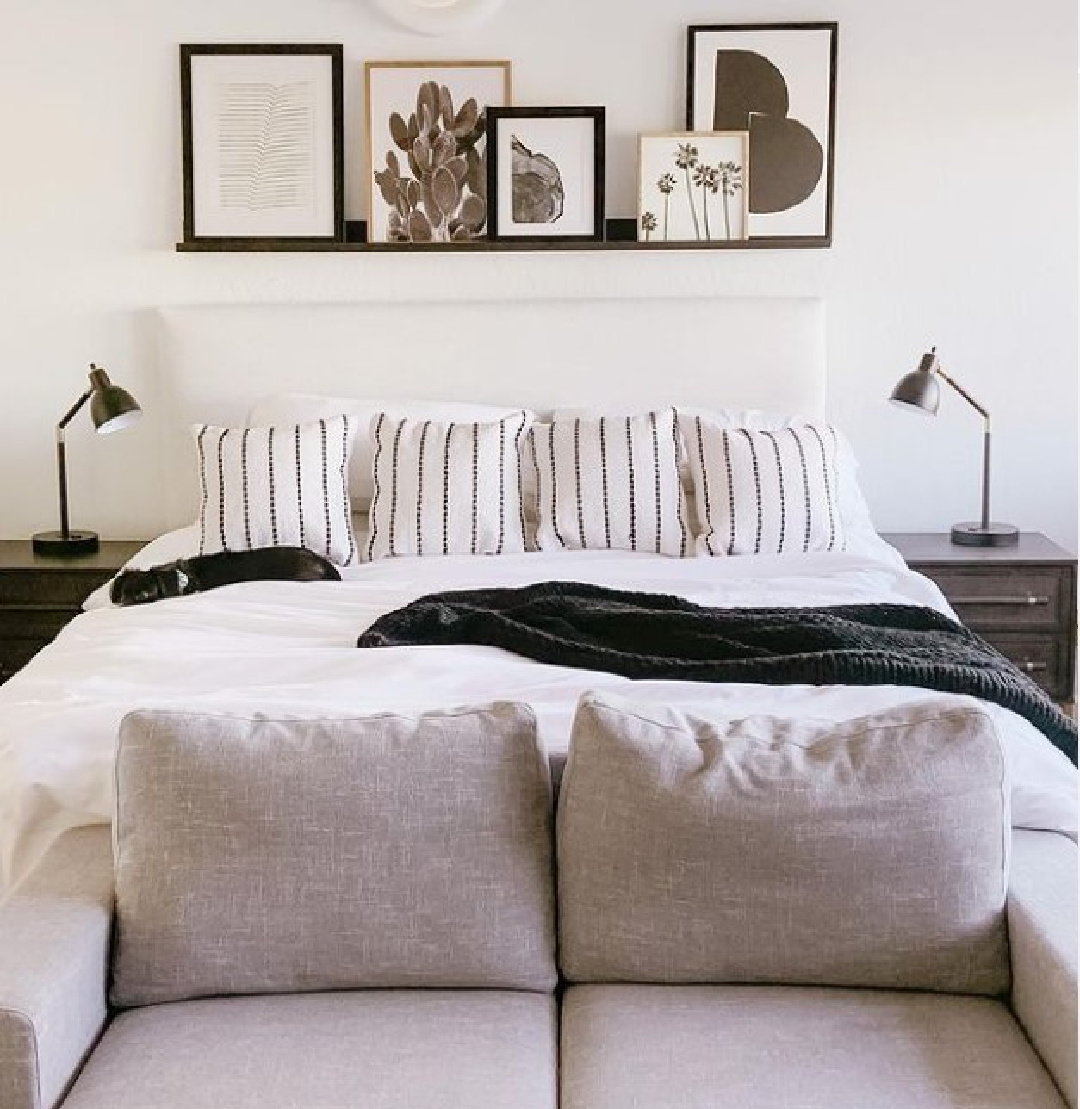 Bedroom with BM Chantilly Lace, loveseat at end of bed, black accents and floating shelf - @theazbeachhouse