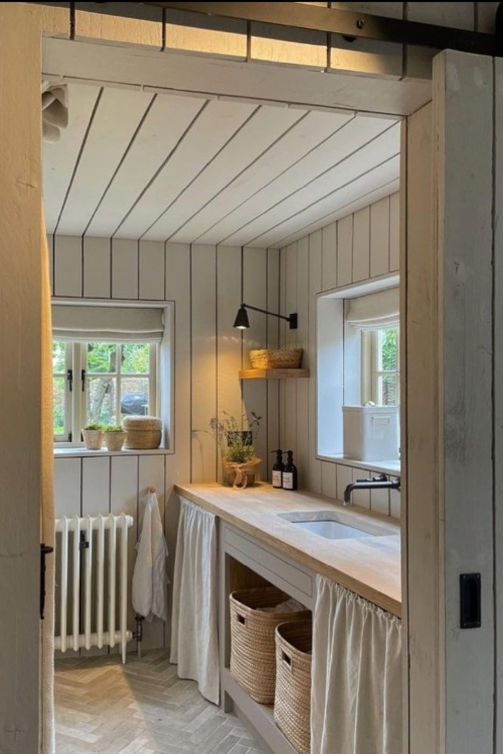 Bee Osborn's charming English country utility room with skirted sink, herringbone floor, and boarded wood walls in a Cotswold cottage - @osborninteriors. #cotswoldcottages #englishcountry