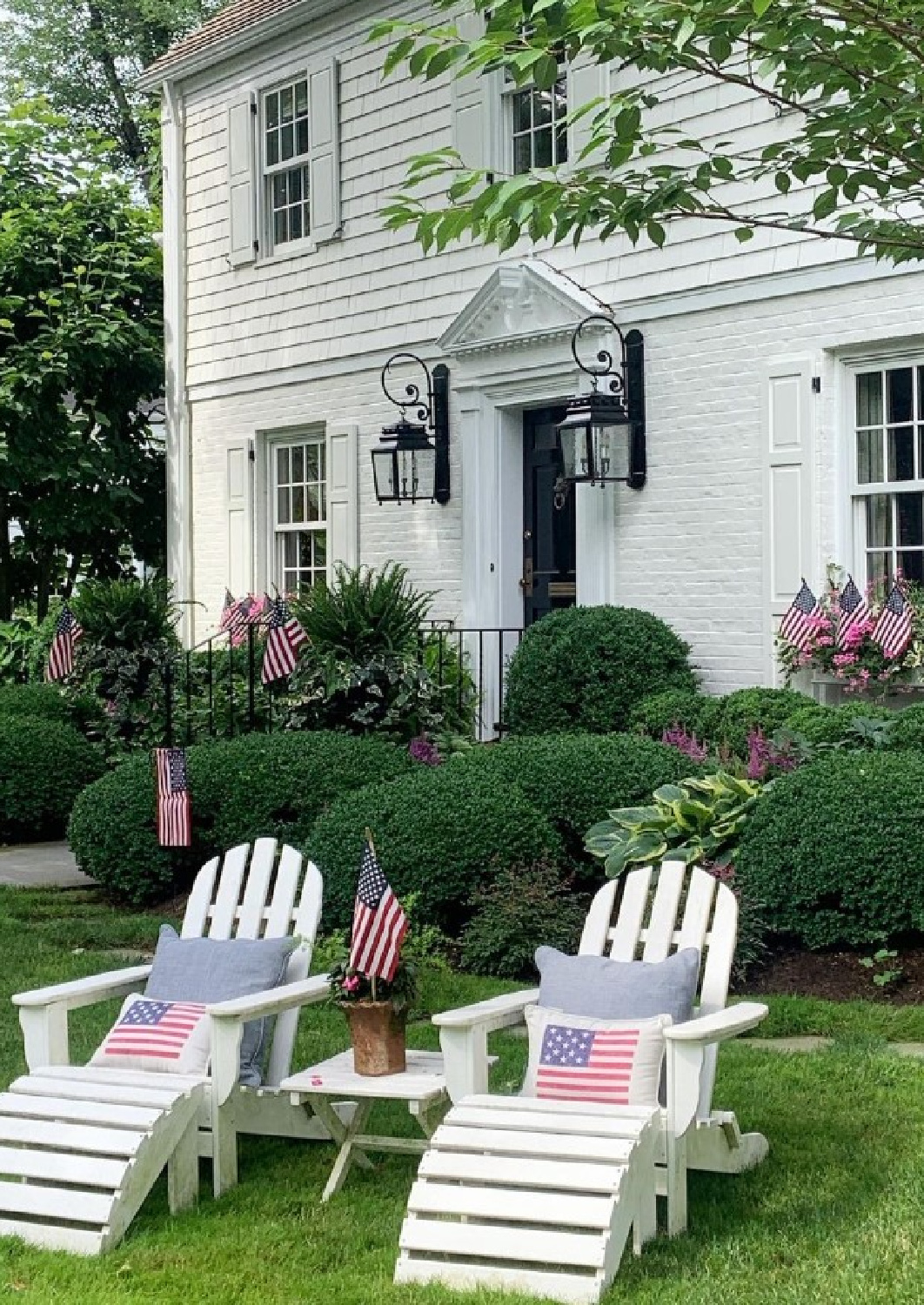 White Dove (Benjamin Moore) painted house with white shutters and Adirondack chairs decorated with American flags for 4th of July - @theprettypinktulips. #bmwhitedove