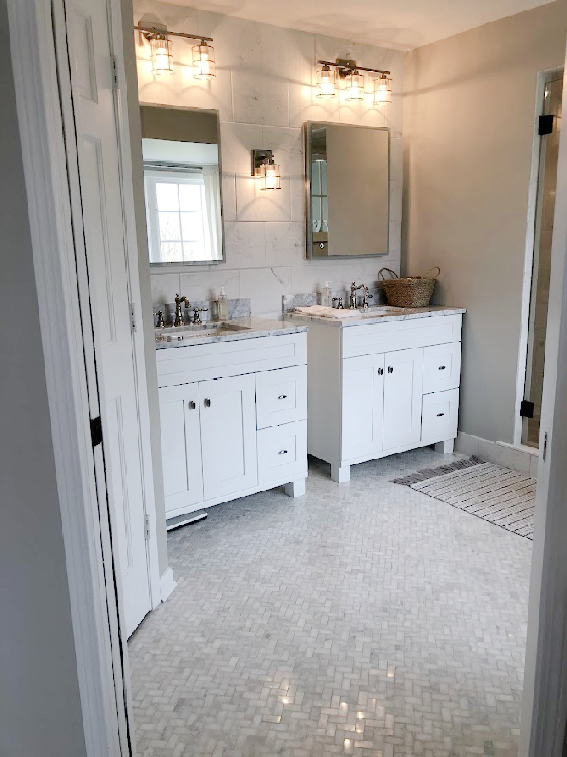 SW Repose Gray on walls, Shaker style white vanities, modern LED medicine cabinets, and white marble mosaic herringbone tiled floor in our modern French renovated bath at the Georgian - Hello Lovely Studio.