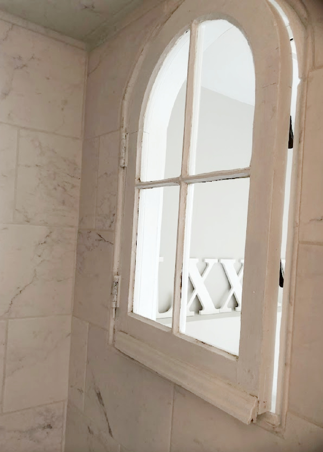 Vintage salvaged arched window with original hardware installed in our renovated shower with marble look porcelain at the Georgian - Hello Lovely Studio.