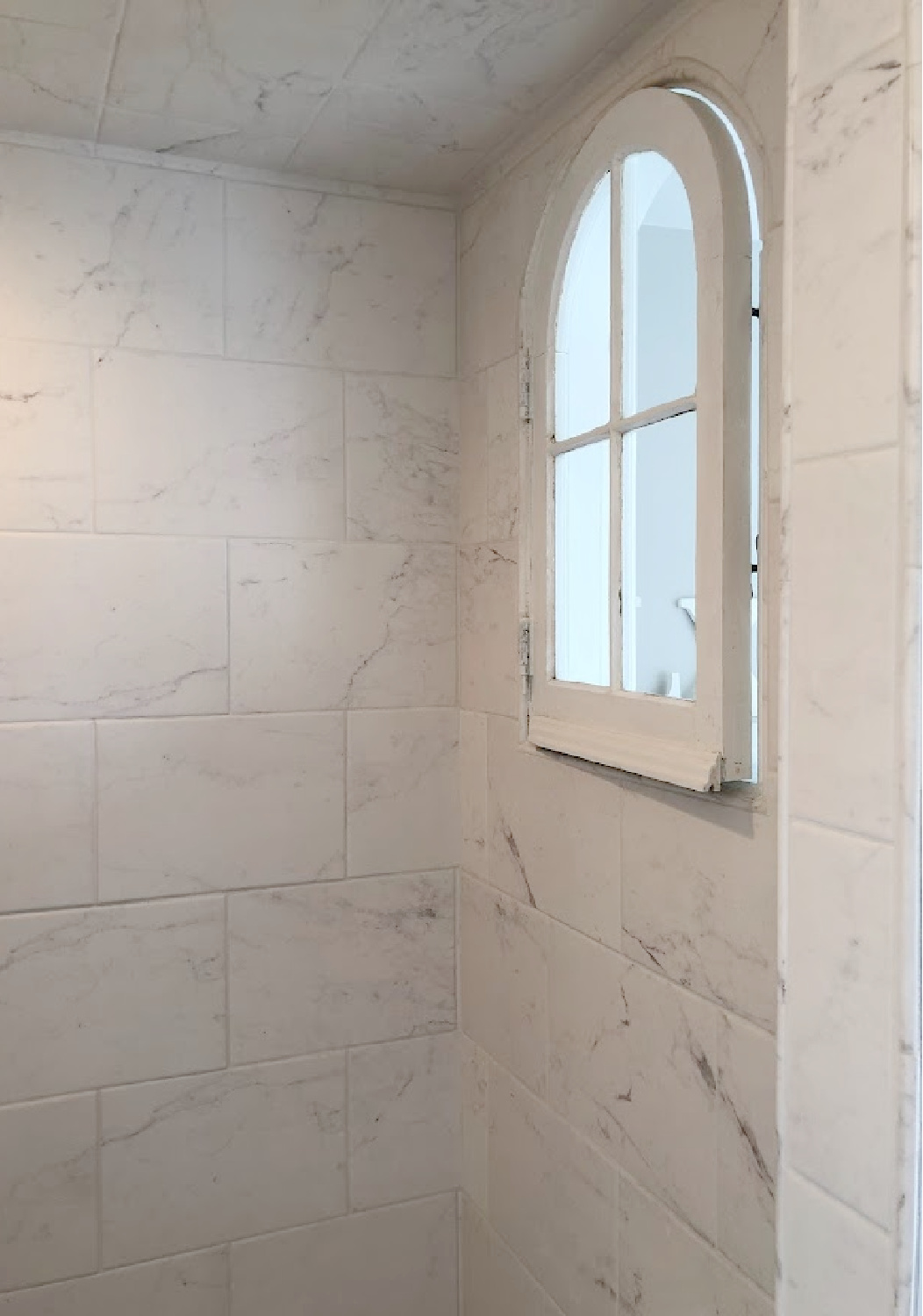 Vintage salvaged arched window with original hardware installed in our renovated shower with marble look porcelain at the Georgian - Hello Lovely Studio.