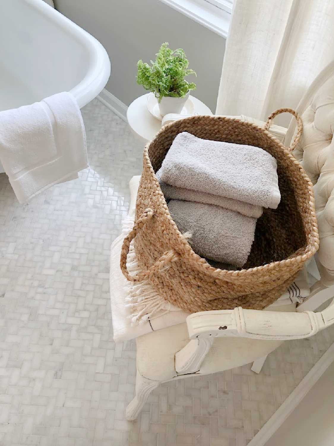 Modern French renovated bath with Louis style arm chair holding basket of towels, column side table with plant, and vintage clawfoot tub - Hello Lovely Studio. Walls are SW Repose Gray. #swreposegray