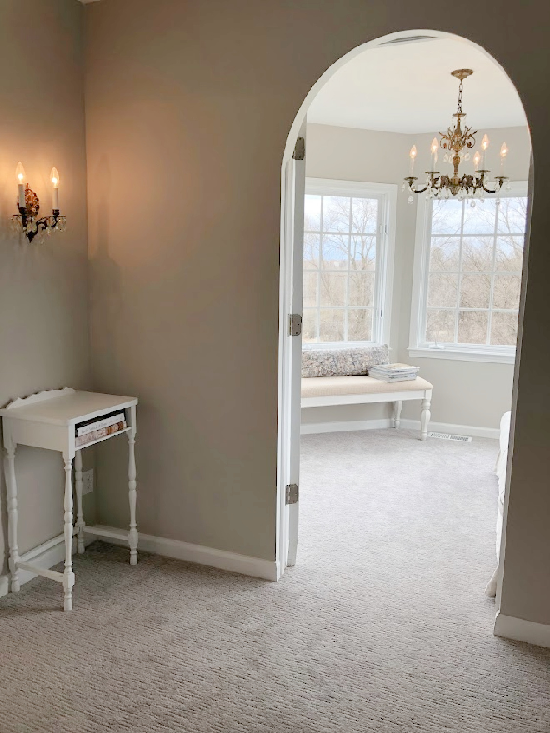 Antique brass double wall sconce, accent table, and arched doorway to sitting room in coastal bedroom remodel (SW Agreeable Gray on walls) at the Georgian - Hello Lovely Studio. #agreeablegray #swagreeablegray