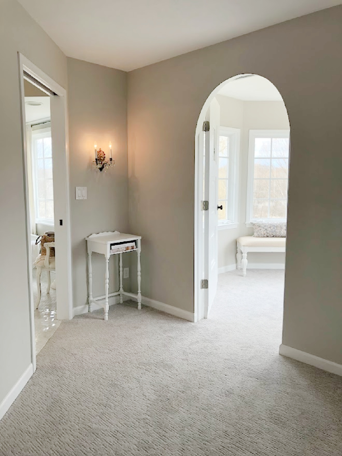 Pocket door to bath, antique wall sconce, and arched doorway to turret sitting room in coastal bedroom remodel (SW Agreeable Gray on walls) at the Georgian - Hello Lovely Studio. #agreeablegray #swagreeablegray