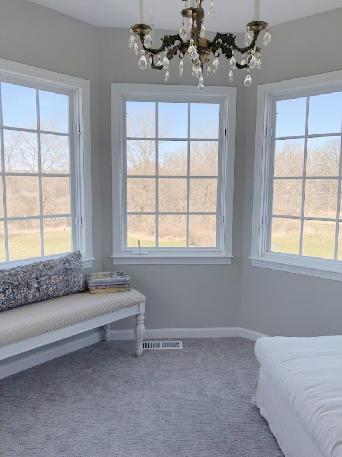 Upholstered bench and crystal chandelier in turret sitting room of coastal bedroom remodel (SW Agreeable Gray on walls) at the Georgian - Hello Lovely Studio. #agreeablegray #swagreeablegray