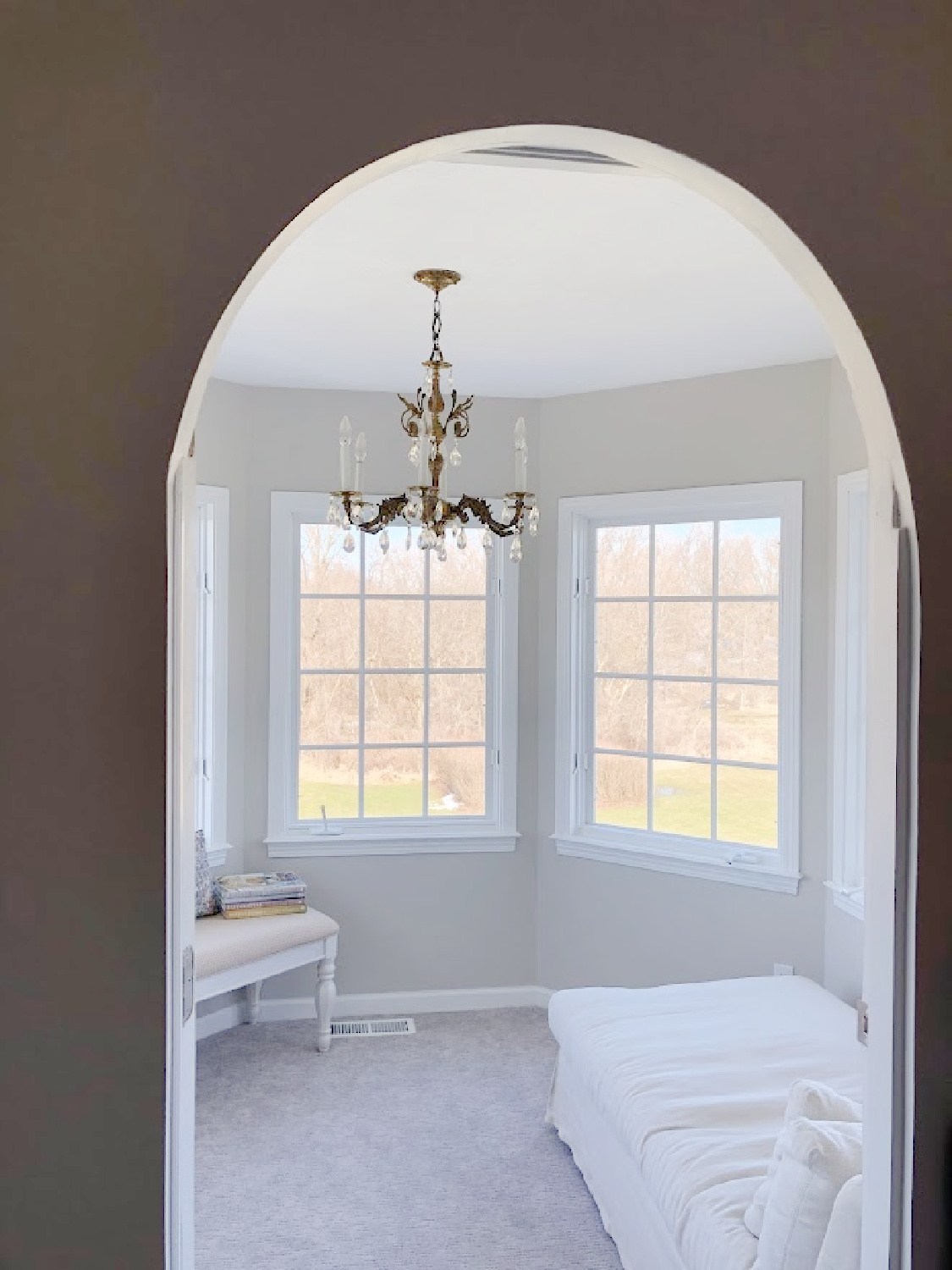 Arched doorway to turret sitting room with chandelier and linen chaise in coastal bedroom remodel (SW Agreeable Gray on walls) at the Georgian - Hello Lovely Studio. #agreeablegray #swagreeablegray