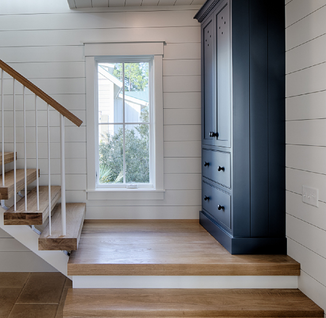 White oak hardwood floor and stairs in entry with shiplap on walls and tall cabinet painted blue. Board and batten coastal cottage in Palmetto Bluff with modern farmhouse interior design by Lisa Furey. #andessummit #benjaminmoore #paintcolors #bluepaintcolors #benjaminmooreandessummit