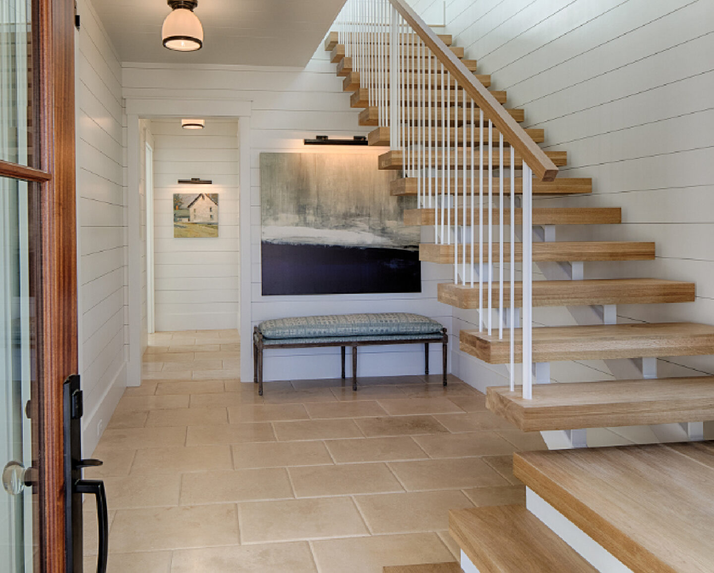 White oak hardwood flooring and floating staircase in entry with shiplap painted Benjamin Moore White. Board and batten coastal cottage in Palmetto Bluff with modern farmhouse interior design by Lisa Furey. #entry #openrisers #staircase #coastalstyle #interiordesign #modernfarmhouse #shiplap