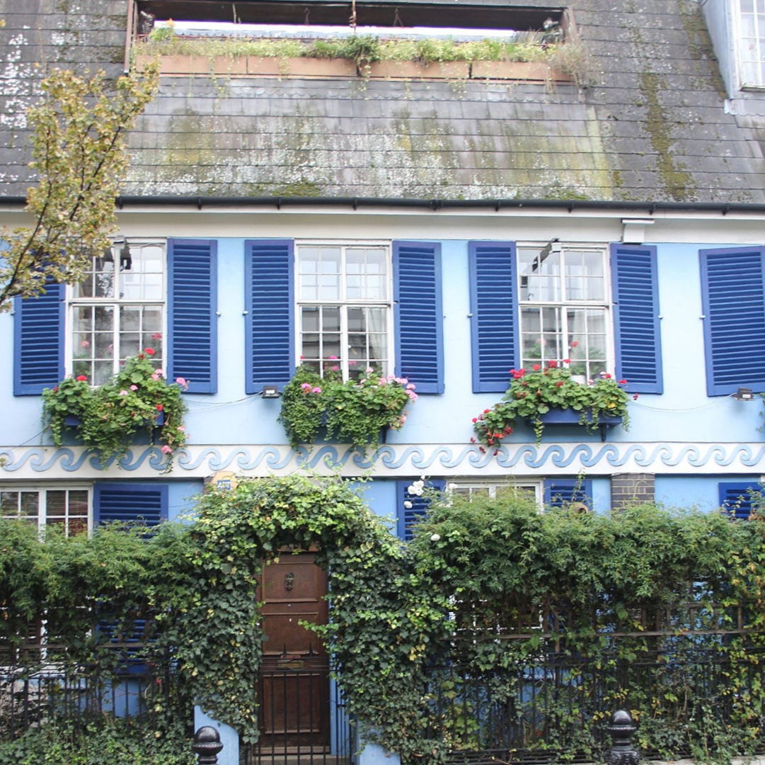 Beautiful sky blue house exterior with royal blue shutters and window boxes in Notting Hill. Come explore paint colors for your front door. #frontdoorcolors #paintcolors #curbappeal