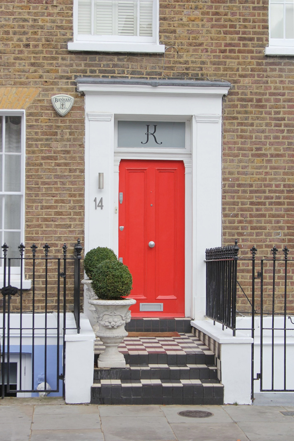 Bold and vibrant red-orange door and brick row house exterior in Notting Hill. Come explore paint colors for your front door. #frontdoorcolors #paintcolors #curbappeal