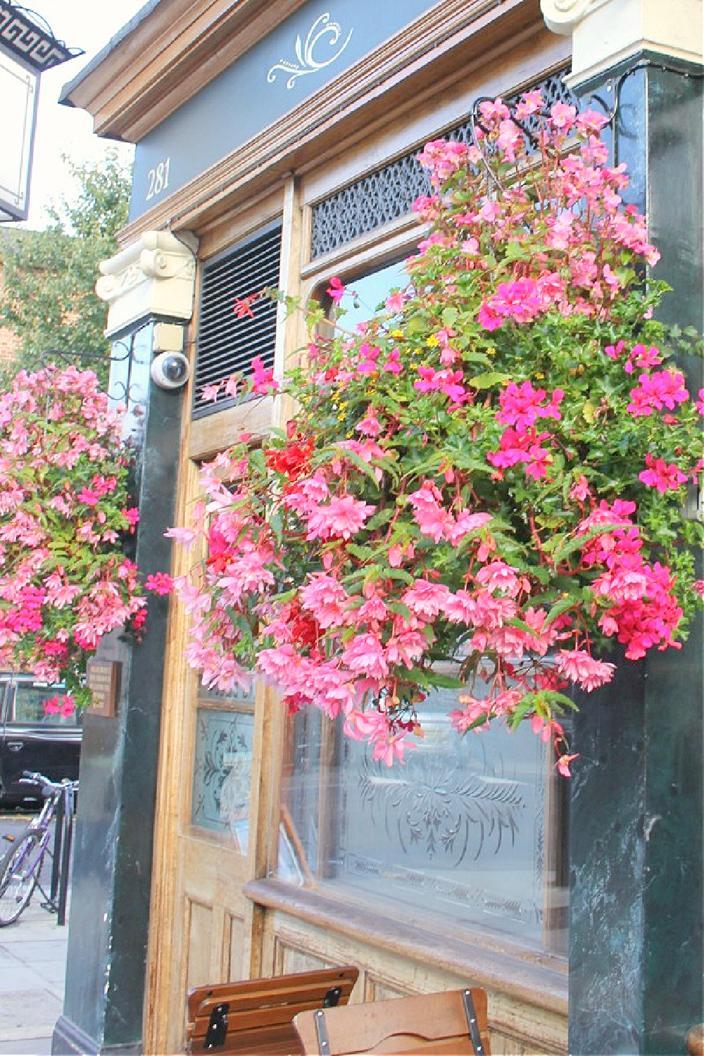 Vibrant pink blooming flowers in hanging baskets outside of a London pub - Hello Lovely Studio.