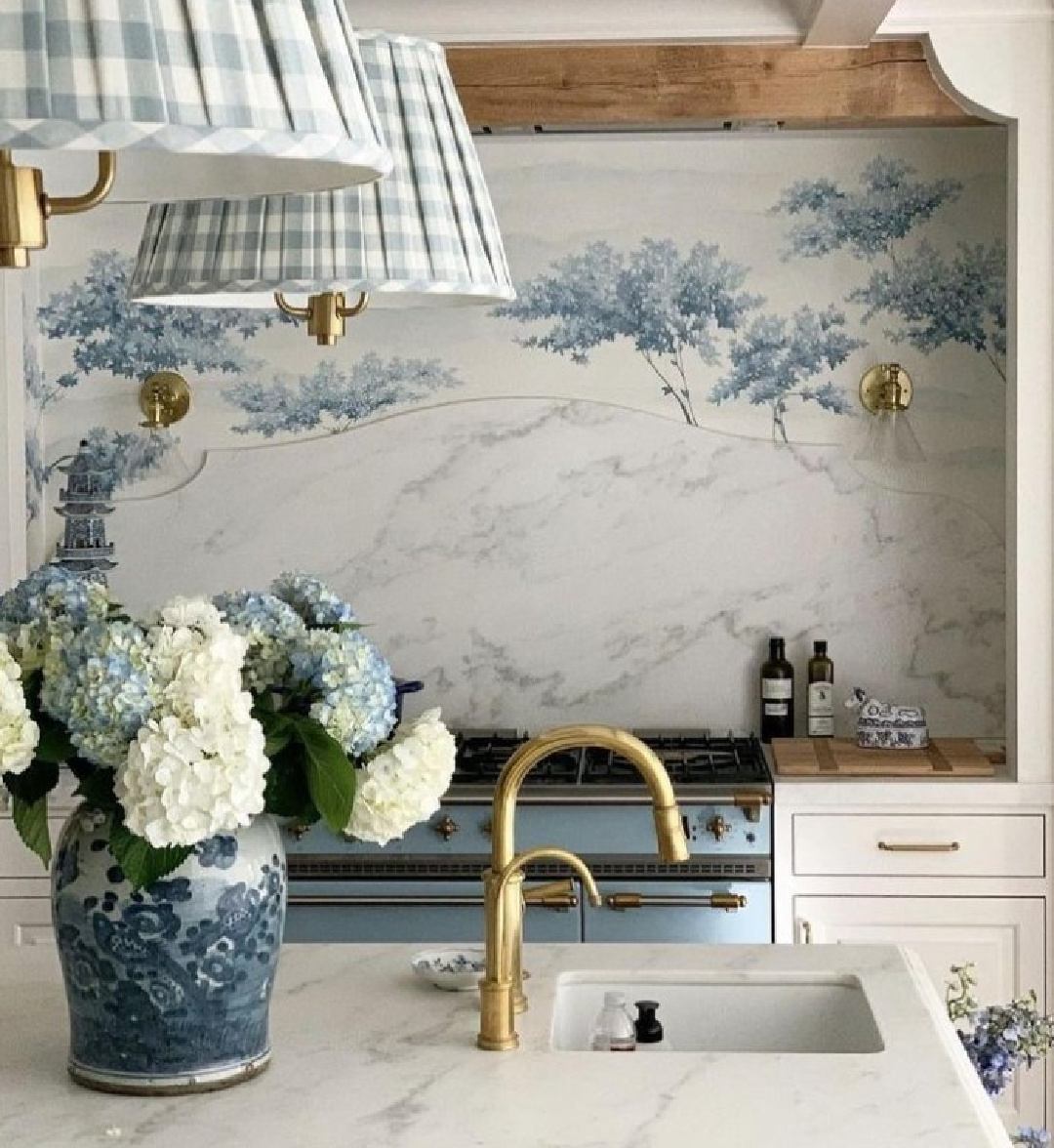 French country kitchen with blue tree mural behind range, gingham pendant shades, blue range, and brass hardware - via style_secrets_magazine. #bluekitchens #frenchcountrykitchen