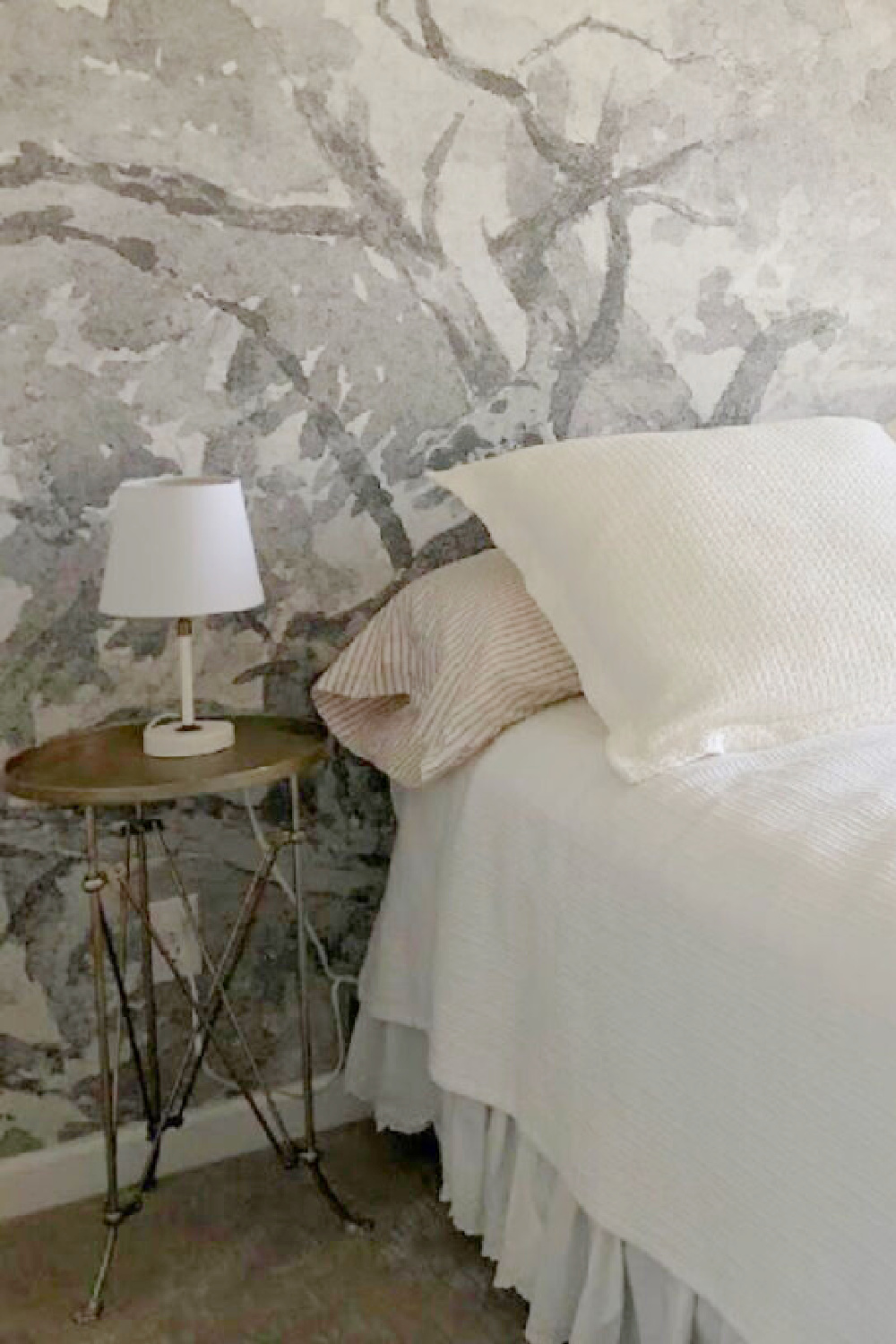 Silver round accent table with mini lamp in bedroom with white bedding and abstract grisaille wallpaper mural from Photowall - Hello Lovely Studio.