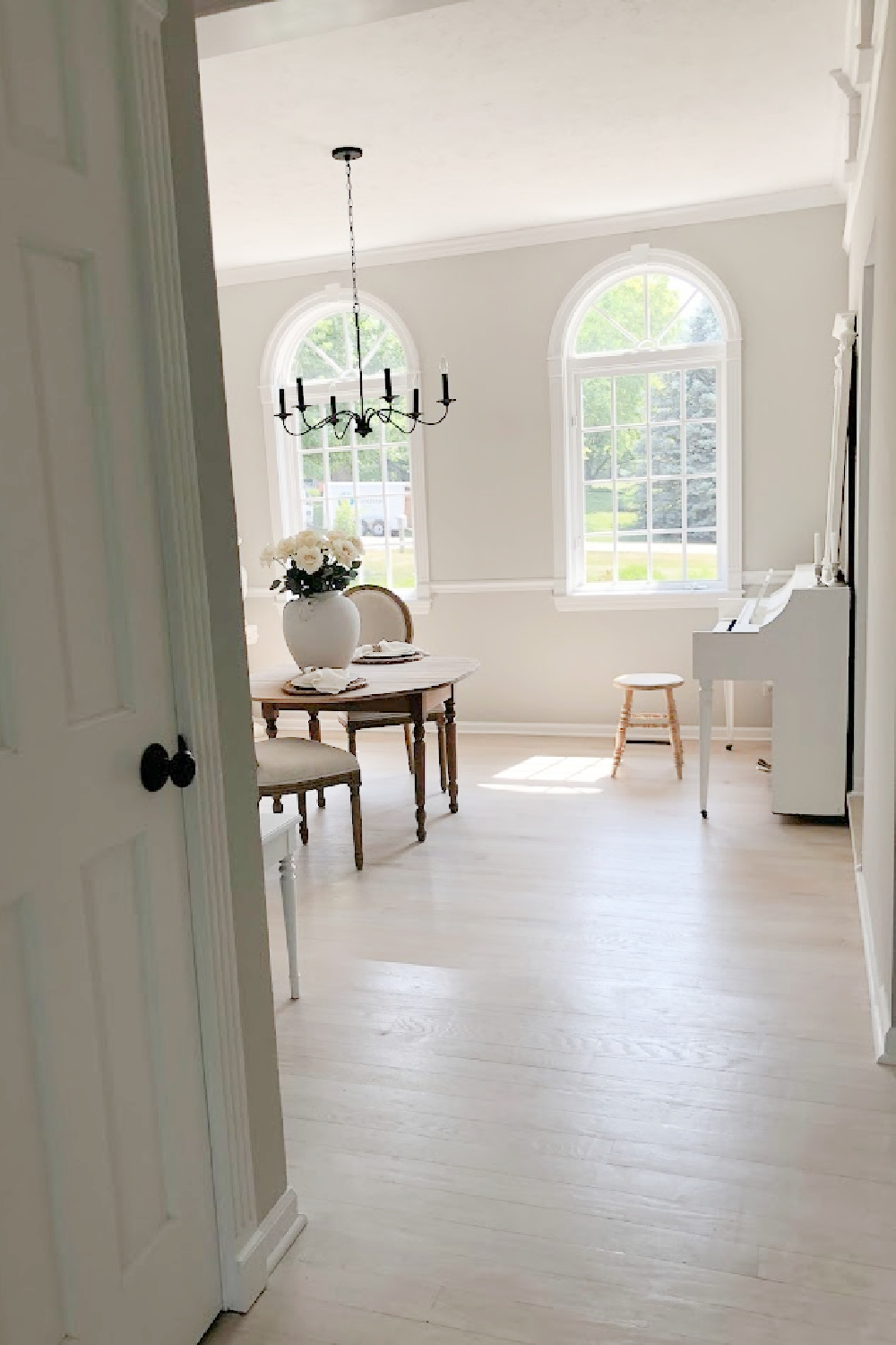 Dining room with light grey stained hardwood floors and white piano - Hello Lovely Studio.