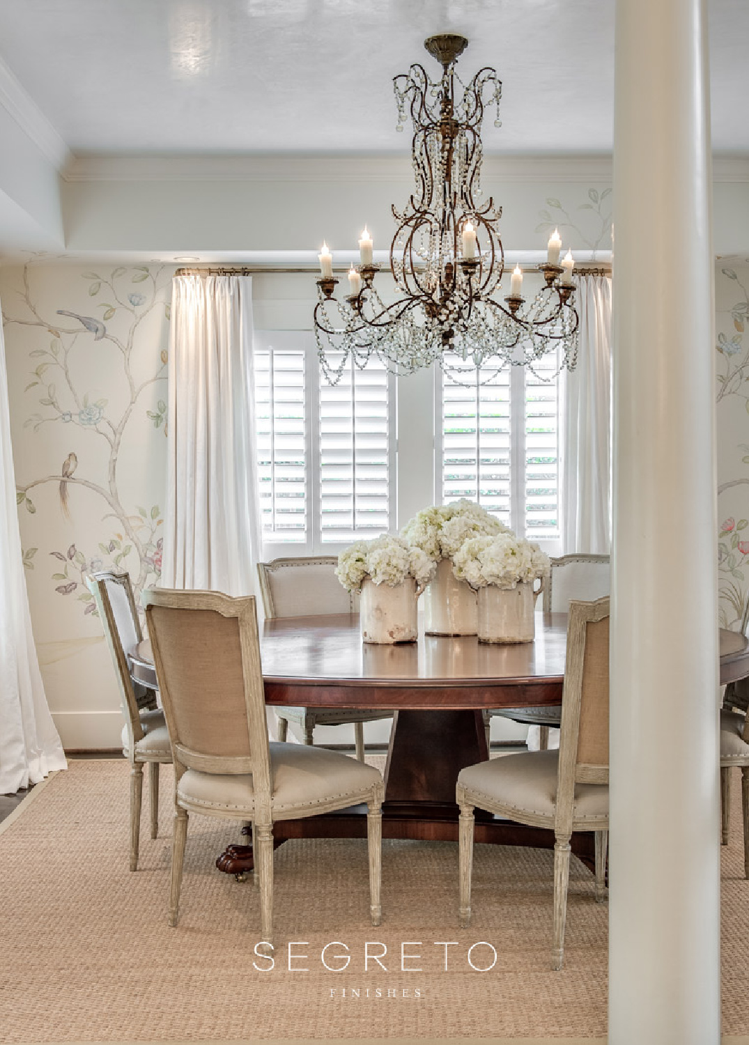 Lovely dining room with mural painted by Segreto Finishes, round pedestal table, and grand chandelier.