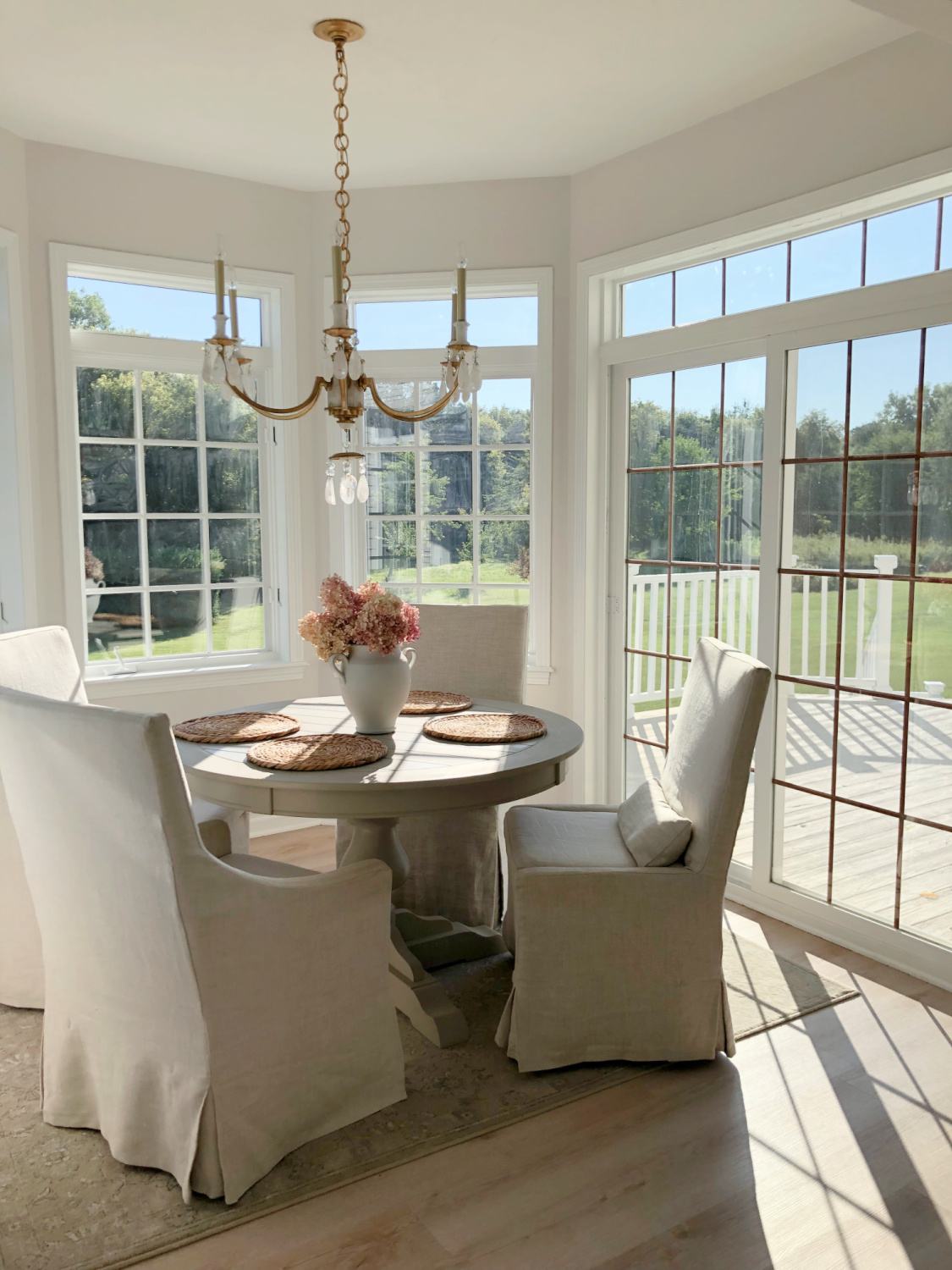 Belgian linen slipcovered dining chairs in serene white breakfast nook with Eider White painted walls - Hello Lovely Studio. #eiderwhite #modernfrench #europeancountry #belgianlinen