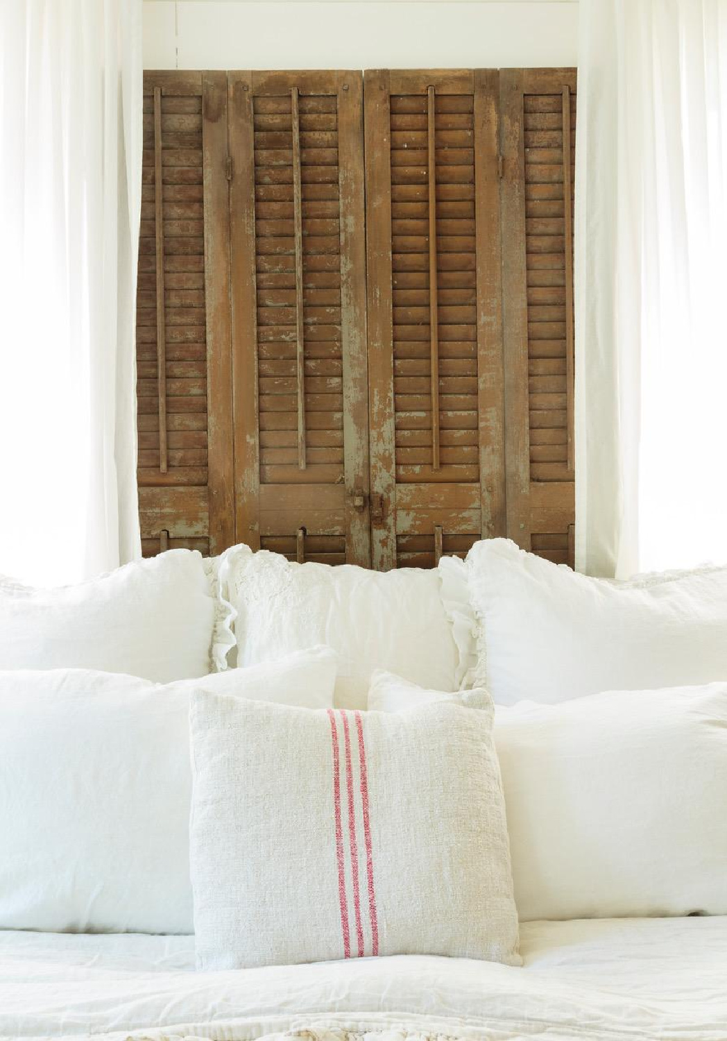 Rustic wood shutters as headboard in a white bedroom from Fifi O'Neill's SHADES OF WHITE (CICO Books, 2021). #fifioneill #whiteinteriors
