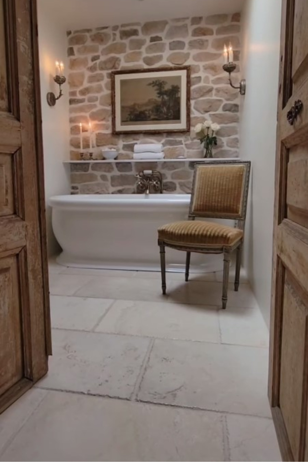 French country bath with stone accent walls, shelf, candles, and luxurious design by @thefrenchnestcointeriordesign. #frenchcountrybath #oldworldstyle
