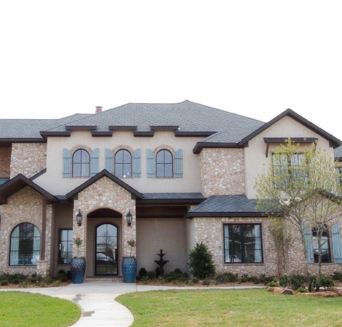 Country French house exterior with pale stone, dark brown trim and French blue shutters - Brit Jones Design.