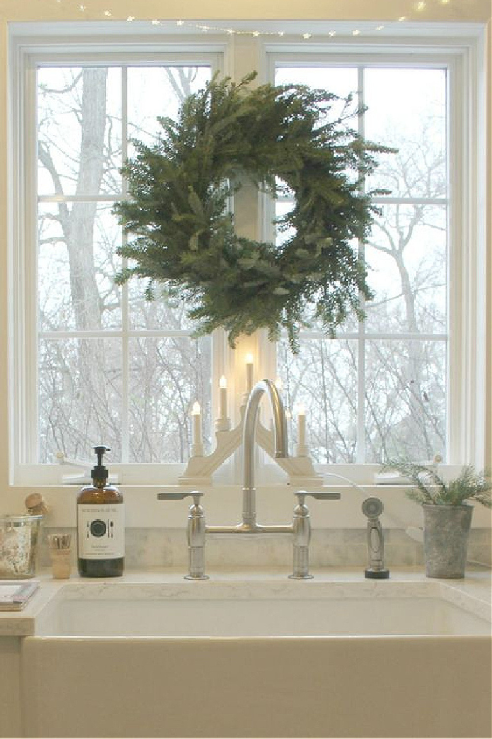 White Scandi Christmas decor in my farmhouse kitchen with Frasier fir wreath and Swedish candelabra at the farm sink in our white kitchen - Hello Lovely Studio. #christmasdecor #christmaswreath #hellolovelystudio #scandichristmas #christmaswreaths #candelabra #swedishchristmas