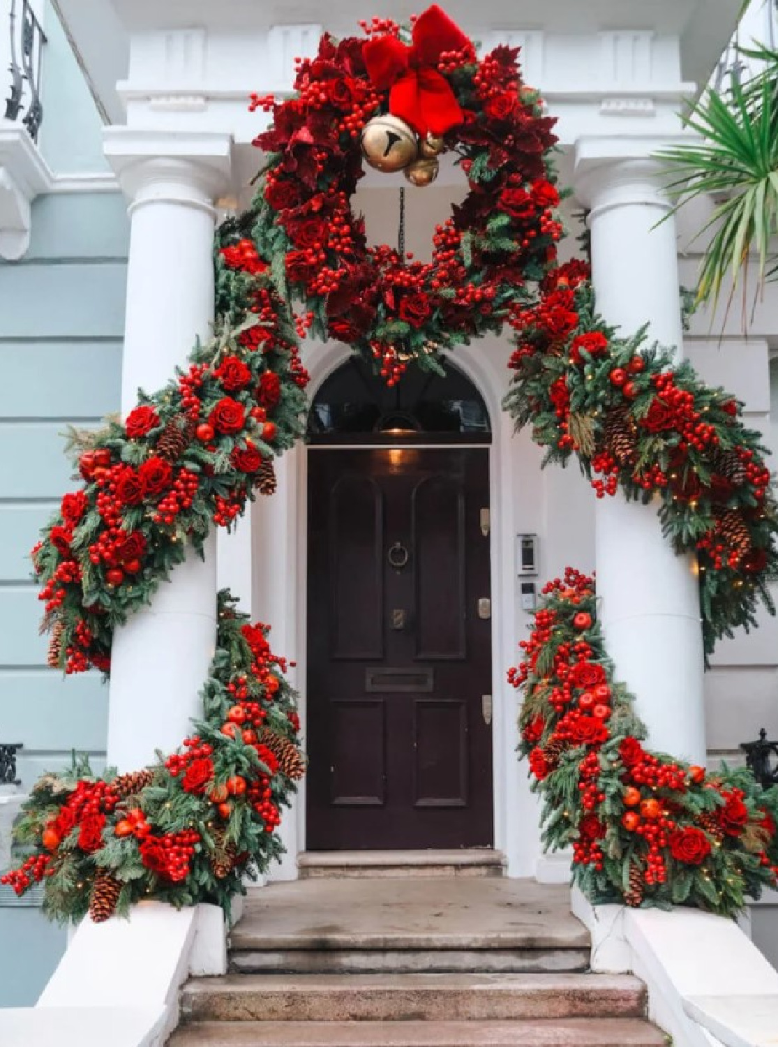 Fanciful Christmas decorated Notting Hill entrance and front door with red garlands and wreath - Jou Jou Travels. #britishchristmas #christmascurbappeal #anglophilechristmas