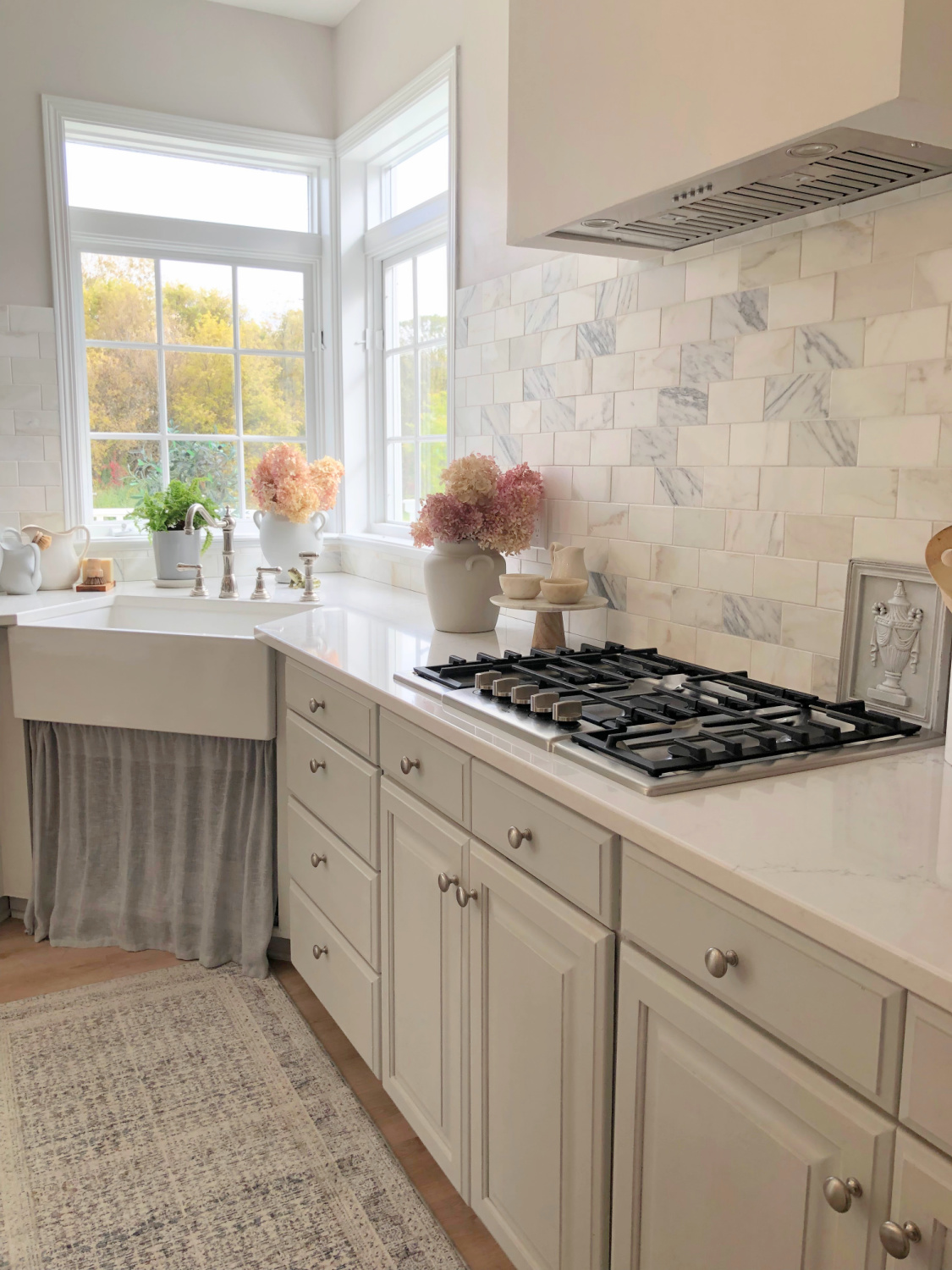 Hello Lovely's modern French serene kitchen (walls are SW Eider White) with F&B Pavilion Gray cabinets, Viatera Muse quartz counters, and farm sink with linen skirt. #modernfrench #timelesskitchens