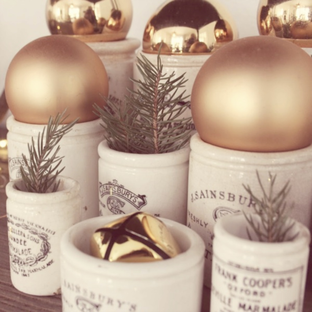 Vintage English crocks filled with gold bulbs, fresh greenery, and bells for Christmas decor - Hello Lovely Studio. #hellolovelychristmas #vintagechristmas #englishcountrychristmas