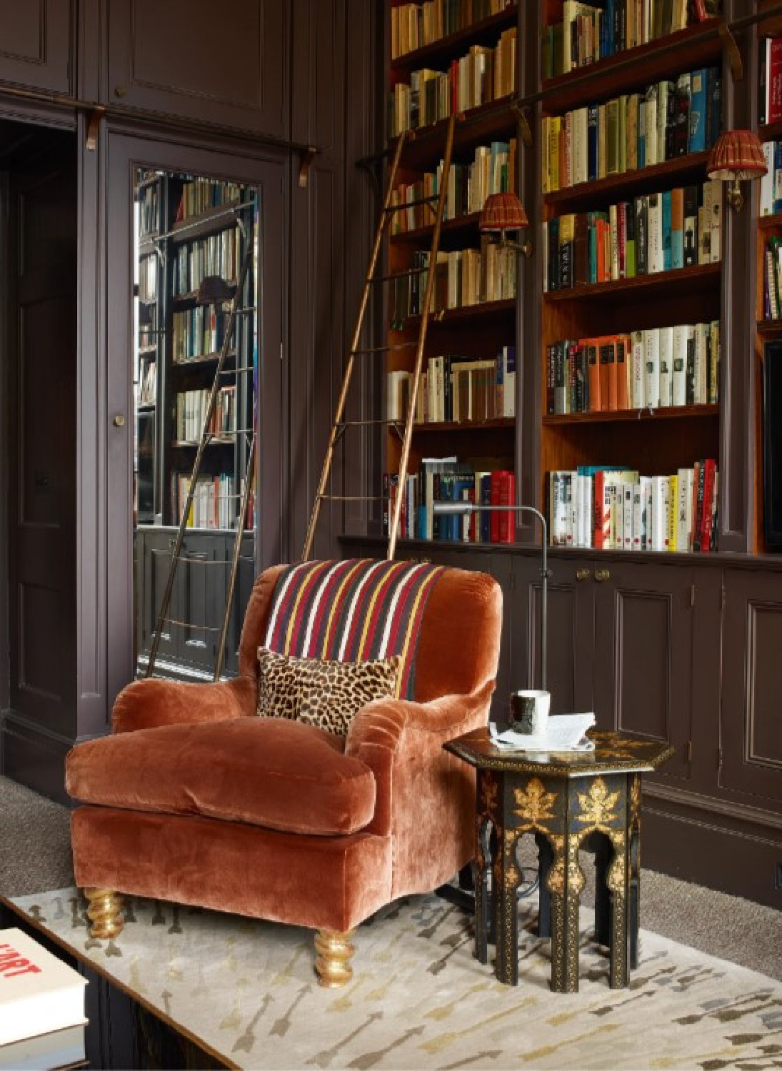 Douglas Mackie designed snug room home library painted dark moody colors with burnt orange velvet arm chair (photo Simon Upton in House & Garden UK). #homelibrary #englishlibrary #snugrooms