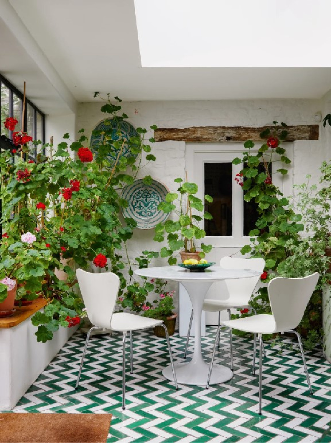 Geraniums in a garden room with green tiles at Cotswold home of Renshaw and Sarah Hiscox in HouseandGardenUK (photo Paul Massey). #cotswoldcottage #englishcountrystyle