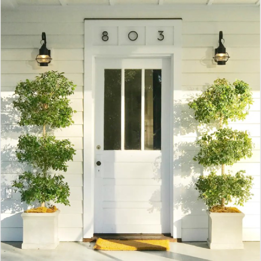 Glidden White High Hide exterior on a low country 1880s cottage with porch, simple lanterns and tall topiaries. #lowcountrycottages #whitecottages #countryporch