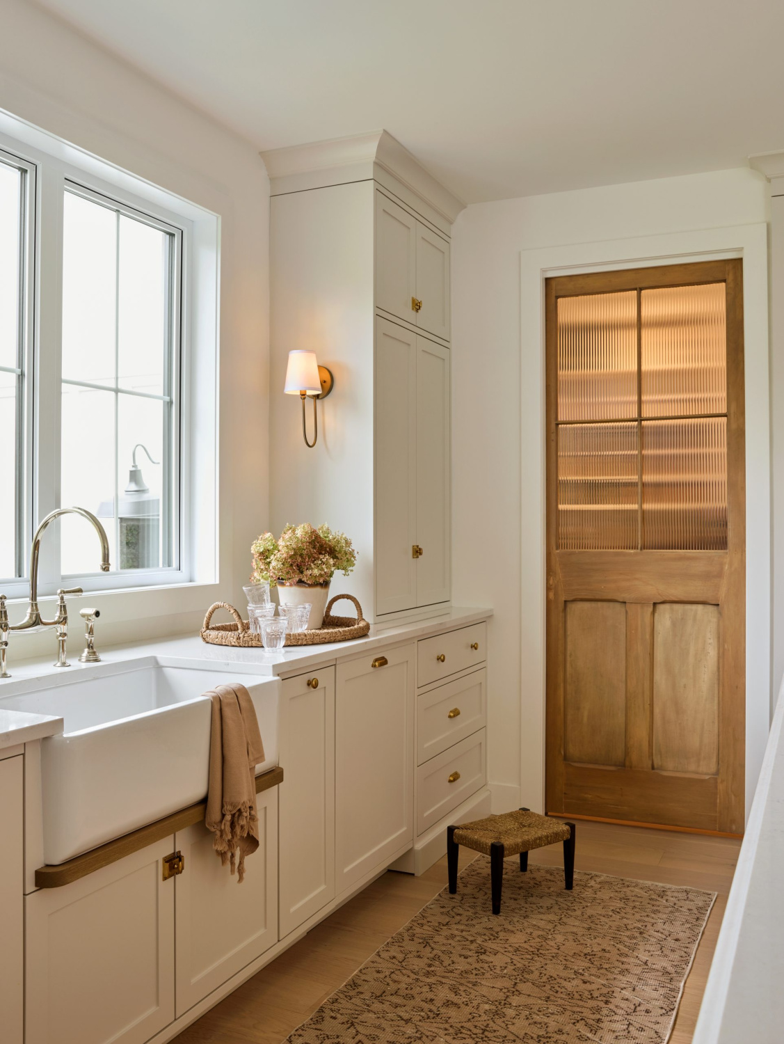 Benjamin Moore Pale Oak in a gorgeous warm white kitchen with wood door to pantry and farm sink - AKB Design. #warmwhitekitchen #kitchendesign