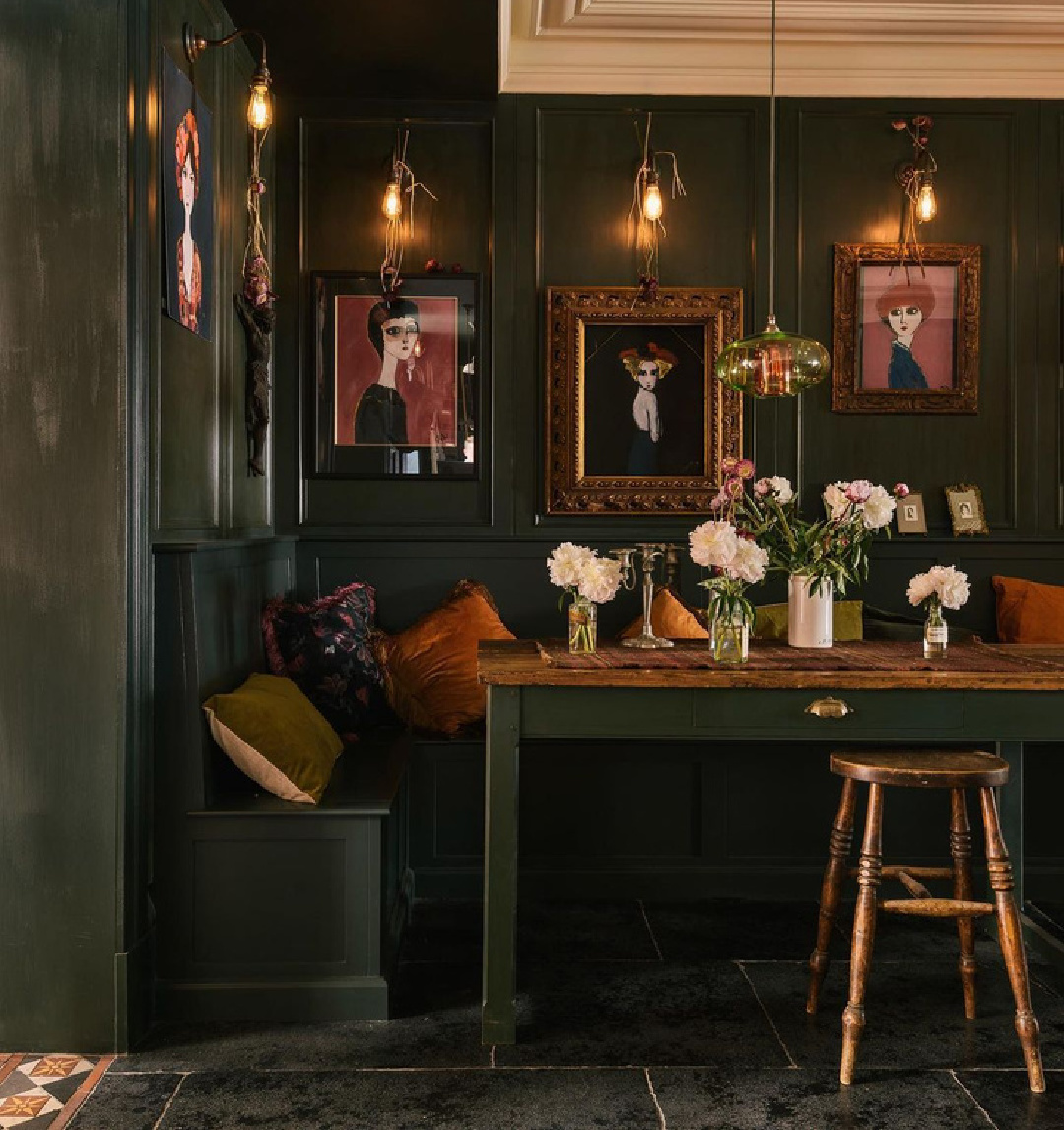 Moody dark green painted paneled walls and furniture in a kitchen dining area with industrial sconces and bespoke design - deVOL.
