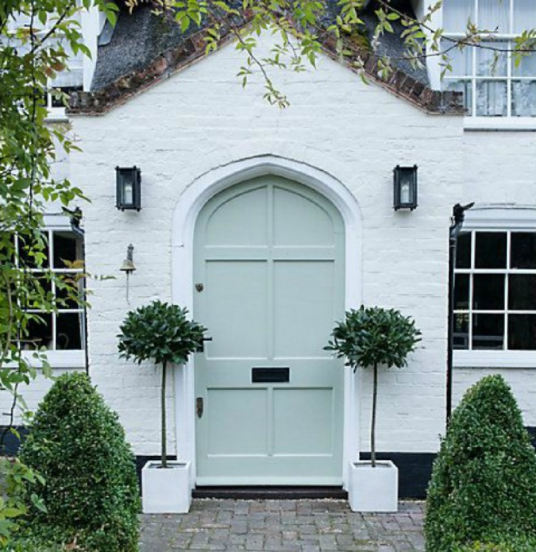 White brick painted English cottage with gray-green door and potted Sweet Bay Trees - Thompson Morgan. #whitebrickhouse #englishcottages #whitecottages