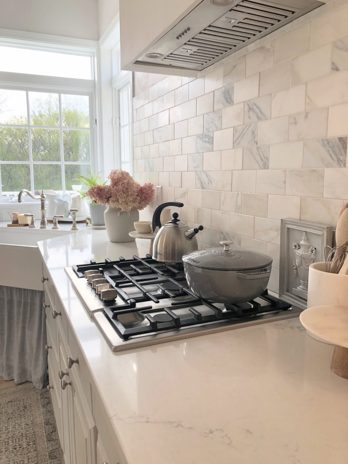 Hello Lovely's light grey and white modern French kitchen with Muse quartz, farm sink, Calacatta marble backsplash and Staub French oven. 
