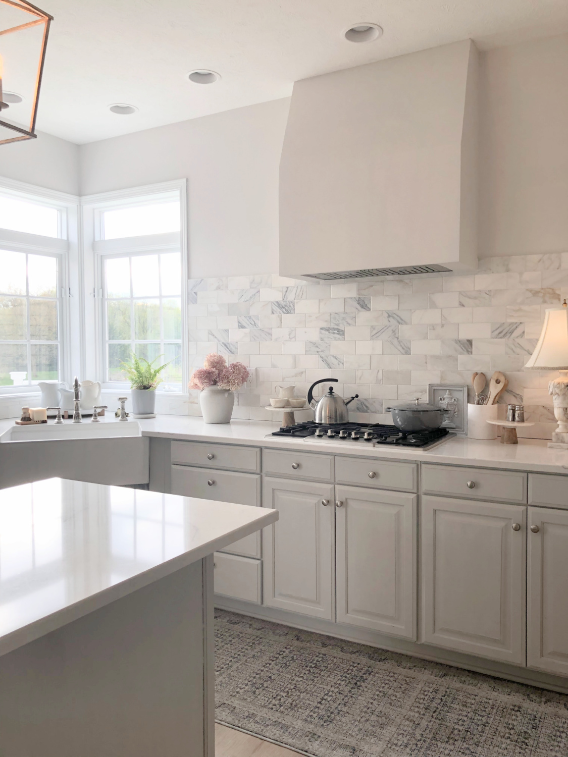 Hello Lovely's light grey and white modern French kitchen with Muse quartz, farm sink, Calacatta marble backsplash and Staub French oven.